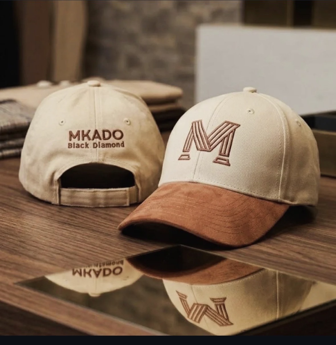 Two cream MKADO Black Diamond caps with tan suede peaks on a wooden table